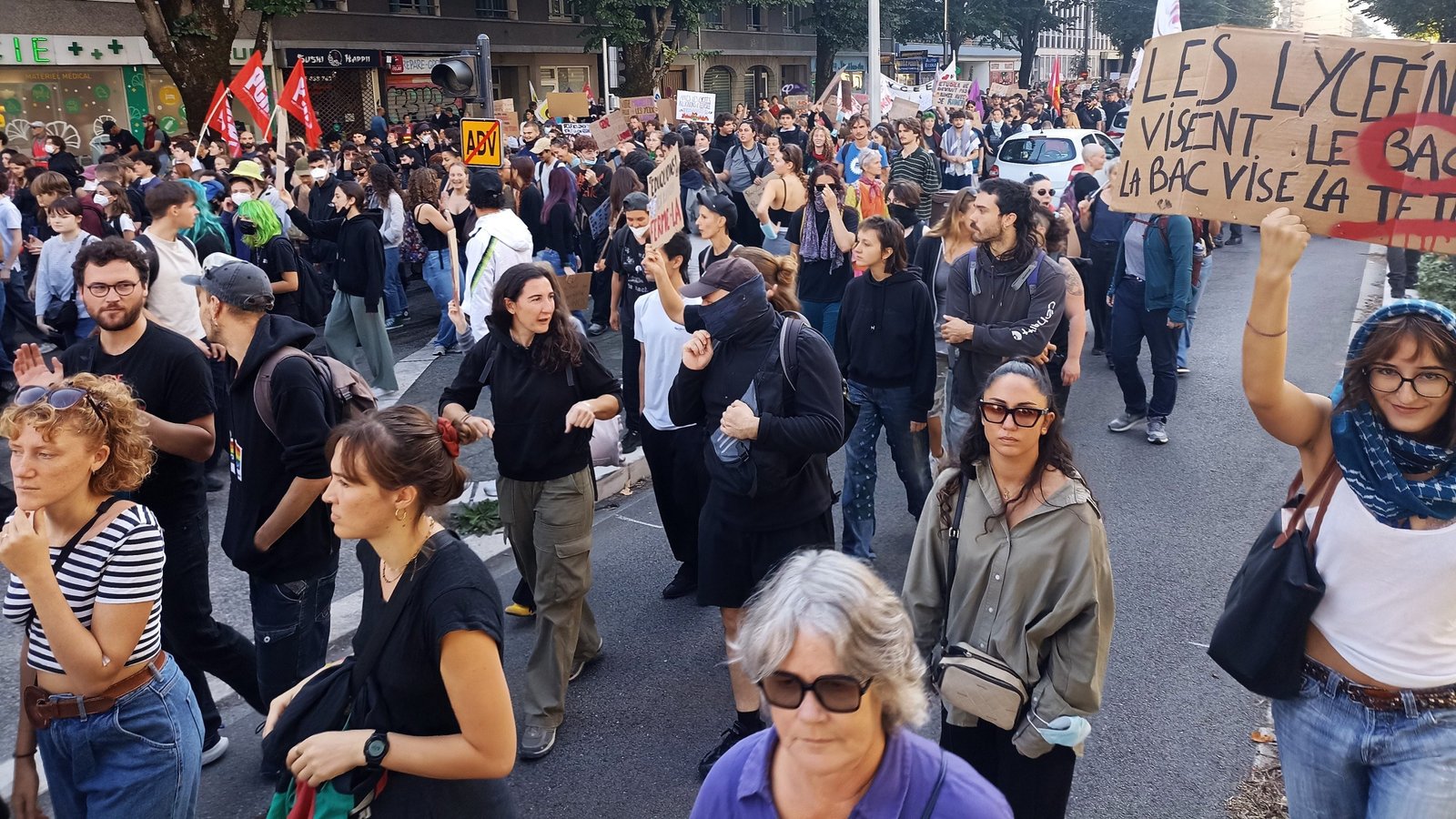 Une foule dense de lycéens et de manifestants défile dans une rue, une pancarte en carton proclamant « Les lycéens visent le bac, la BAC vise la tête ».