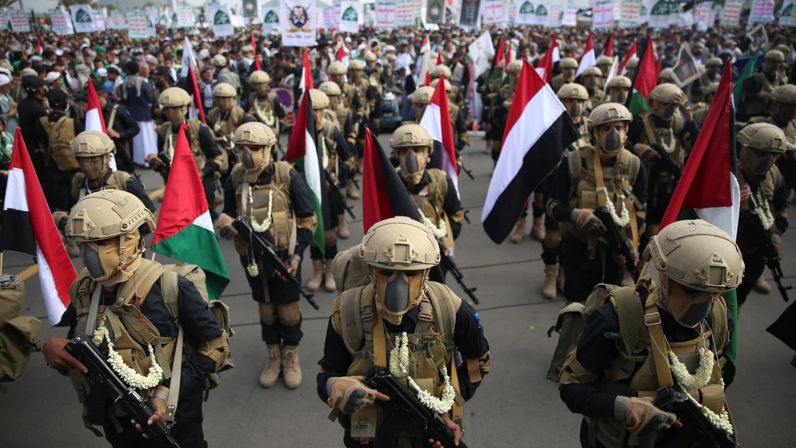 Des combattants houthis casqués, portant masques à gaz et guirlandes de fleurs blanches, défilent armés de fusils d'assaut, brandissant les drapeaux du Yémen et de la Palestine, lors d'un rassemblement du mouvement.
