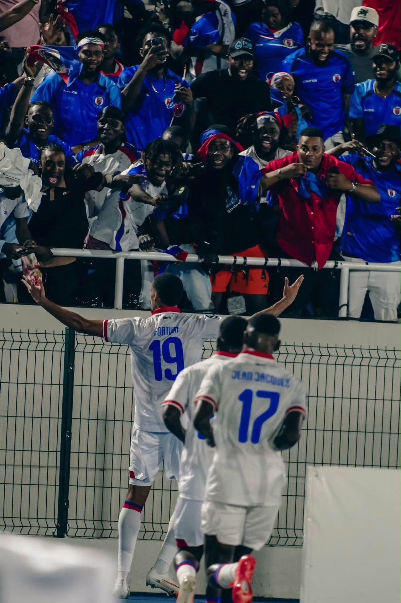 Des supporters haïtiens en liesse, drapeaux et maillots bleu et rouge brandis, acclament les joueurs des Grenadiers au bord du terrain après la victoire 4-1 face à la République dominicaine.